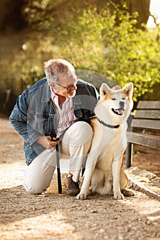 Happy european old man in casual with beard enjoy walk with his dog in park, petting pet outdoor