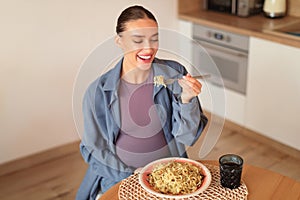 Happy european pregnant woman savoring homemade pasta, enjoy eating spaghetti, sitting at table in kitchen, above view