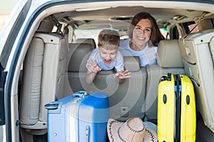 Happy European woman with her little son look back at the trunk of a car with suitcases. Family summer vacation