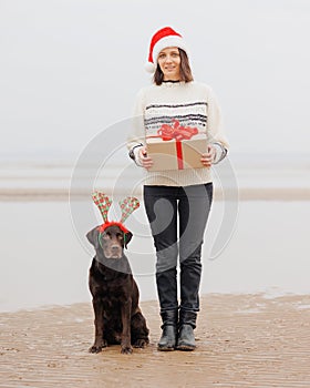 a happy European woman in a Santa Claus hat holds a gift in a box with a red ribbon and her labrador dog in a deer
