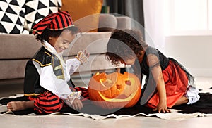 Happy excited african little boy and girl sitting on floor and playing with big jack-o-lantern