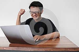 Happy excited Asian man with laptop and raising his arm up to celebrate success or achievement