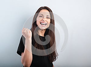 Happy excited beautiful woman showing success triumph sign by fist and loud shouting with open mouth on blue background with empty