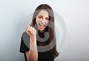 Happy excited beautiful woman showing success triumph sign by fist and loud shouting with open mouth on blue background with empty