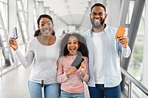 Happy excited black family traveling, holding documents in airport