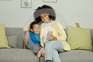 Happy Excited Black Mom And Little Son With Smartphone Celebrate Success By Playing Video Games At Home