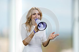 Happy excited blonde middle aged business woman in white dress gives a speech in megaphone.