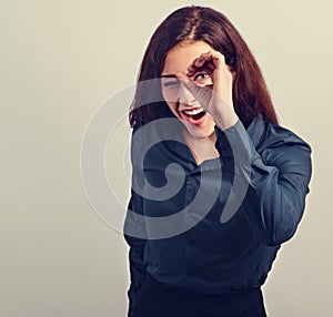 Happy excited business brunette woman doing spyglass sign looking in fingers near the eye in office clothing, shirt and skirt.