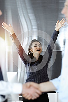 Happy and excited business woman raising hands because of success agreement at meeting. Two men shaking hands in sinny