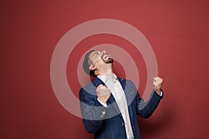 Happy excited businessman shakes clenched fists on red studio background