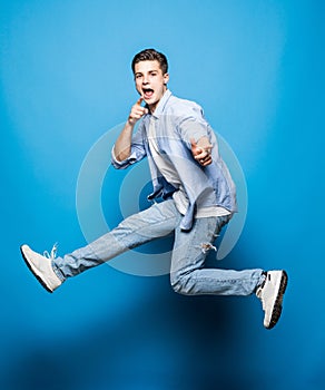 Happy excited cheerful young man jumping and celebrating success isolated on blue background