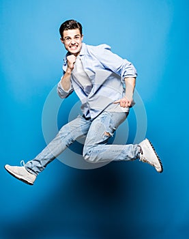 Happy excited cheerful young man jumping and celebrating success isolated on blue background