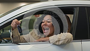 Happy excited client buyer customer smiling African American ethnic woman inside new car showing keys to camera smile