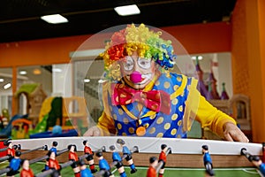 Happy excited clown with funny makeup playing table football