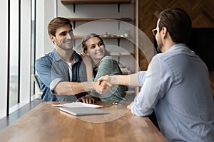 Happy excited couple of clients and lawyer giving handshakes