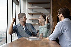 Happy excited couple feeling joy in realtor office, getting mortgage