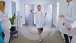 Happy and excited doctors and nurses with a large smile dancing in front of the camera in a modern hospital corridor. 4k