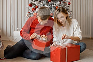 Happy excited family couple unwrap christmas present box on holiday morning in beautiful room near decorated tree