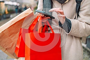 Happy excited female shopper hand holding red blank shopping bags used phone on the city street near the shopping center