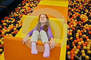 Happy excited girl child crawling in pool with balls at recreation center