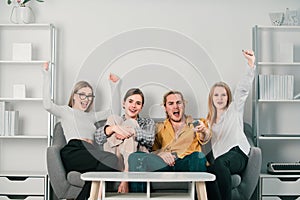 Happy excited group watching television and supporting their team celebrating victory. Group of young people sitting on