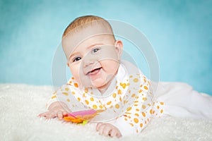 Happy excited infant baby girl lying on the bed with white fur on bright blue background