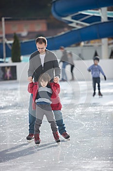 Happy excited little boy and his young father learning ice-skating