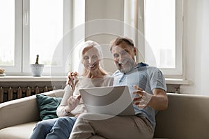 Happy excited mature couple using laptop at home