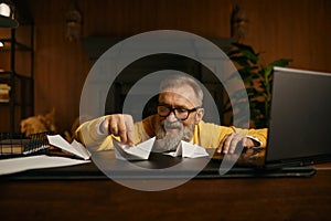 Happy excited mature grey-haired man playing with paper boat at workplace