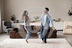 Happy excited millennial couple dancing together in living room