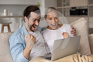 Happy excited millennial couple with digital device celebrating success