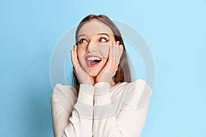 Happy and excited. Portrait of young, smiling, beautiful girl in casual clothes posing over blue studio background