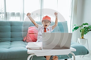 excited primary school student with uniform raise her arm during online class