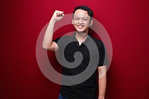 Happy excited and smiling young Asian man raising his arm up to celebrate success or achievement