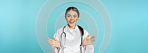 Happy and excited smiling young woman looking with excitement and surprised, standing in white lab coat and stethoscope