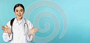 Happy and excited smiling young woman looking with excitement and surprised, standing in white lab coat and stethoscope