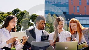 Happy and excited students multiracial studying together on the park in the college territory they using laptops and