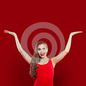 Happy excited surprised woman in red dress having fun on red colorful bright background. Girl with empty hands up