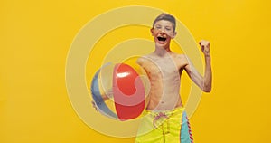 Happy excited teen guy standing with a beach ball isolated on a yellow