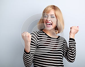 Happy excited winner with opened mouth. Happy blond young satisfacted woman showing the gesture by fists