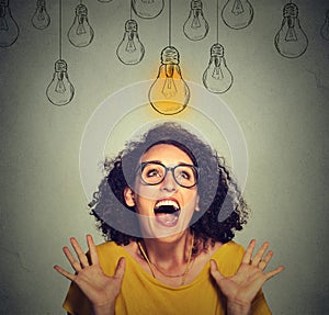 Happy excited woman in glasses looking up at bright light idea bulb above head
