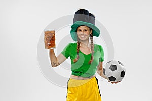 Happy excited woman in green yellow football kit holding beer mug and football ball supports favorite team. Soccer fans