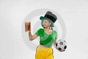 Happy excited woman in green yellow football kit holding beer mug and football ball supports favorite team. Soccer fans