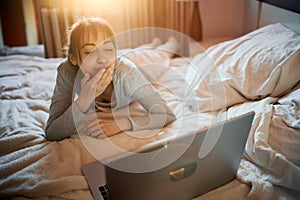 Happy excited woman having video chat online, using laptop camera, send air kiss to boyfriend while lying on bed at home