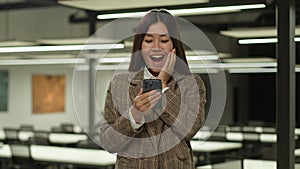 Happy excited wonder Asian woman business student girl looking at mobile phone achieve good news amazing message