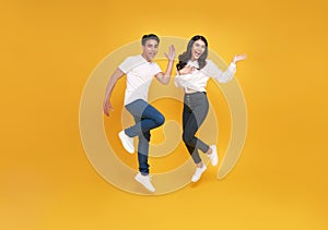 Happy excited young asian loving couple jumping isolated over yellow wall background