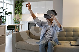 Happy excited young black woman enjoying virtual reality shopping experience while resting at home