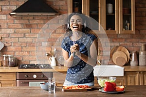 Happy excited young Black woman having fun in kitchen