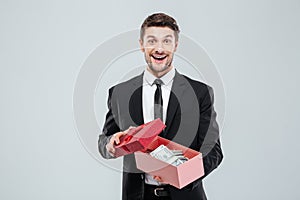 Happy excited young businessman holding gift box full of money