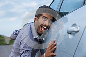 Happy excited young indian man driver embracing petting his car. Green energy biofuel electric environment friendly new car